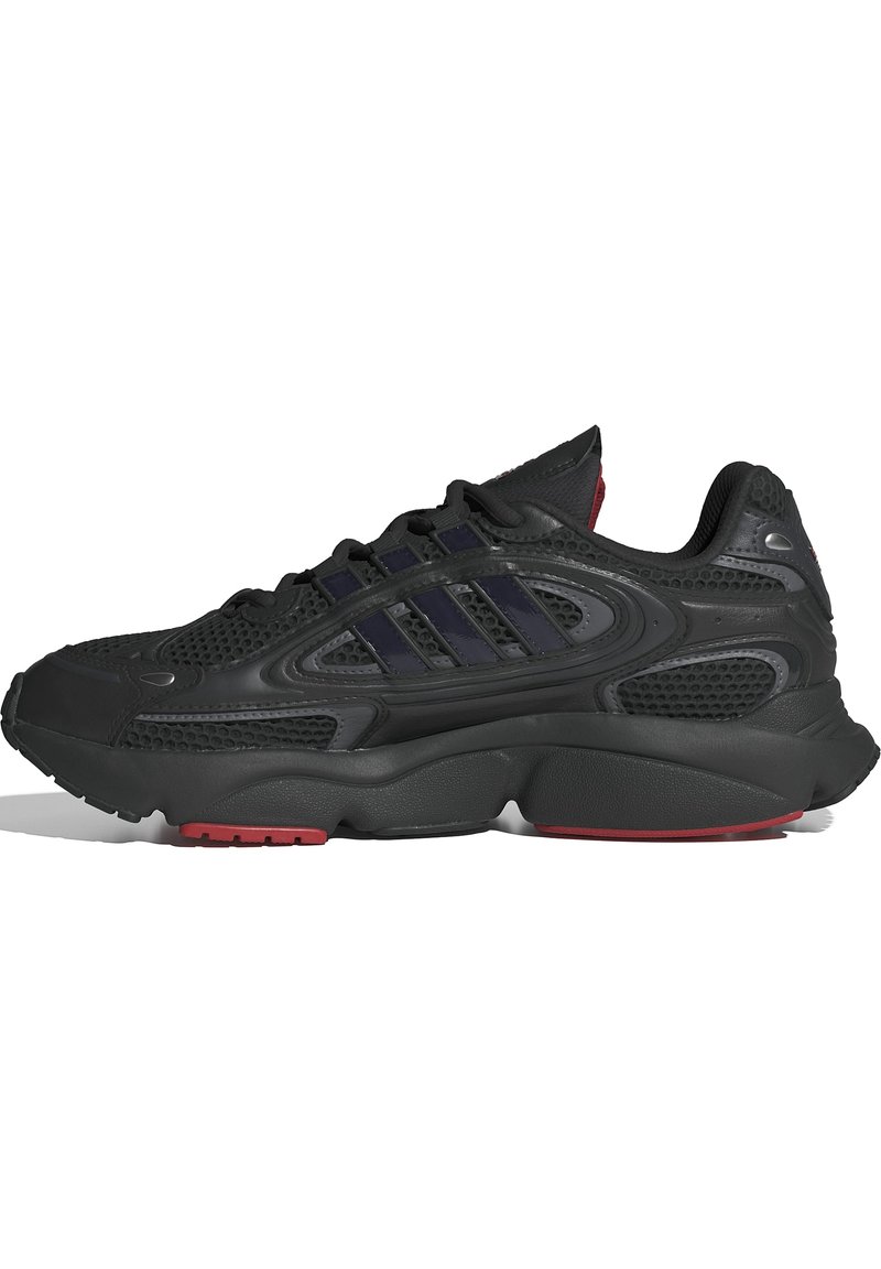 Scarpa da ginnastica nera con upper in rete e sintetico, caratterizzata da tre strisce blu scuro, suola testurizzata e accenti rossi sulla suola esterna.