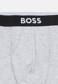 Γκρι βαμβακερά εσώρουχα μποξέρ με μαύρη ελαστική μέση που φέρει το λογότυπο "BOSS" σε λευκό. Μαλακή υφή με λεπτομέρειες ενισχυμένης ραφής.
