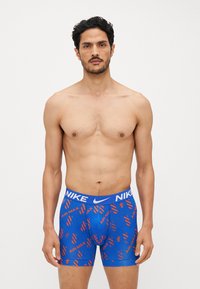 Modri bokserice z elastičnim pasom, na katerem je Nike logo, okrašene z rdečimi abstraktnimi vzorci.