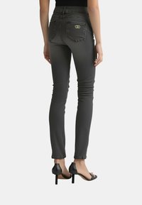 Jeans grigi slim-fit con una texture liscia, dotati di tasche posteriori e dettagli in metallo dorato, abbinati a sandali neri con tacco alto.