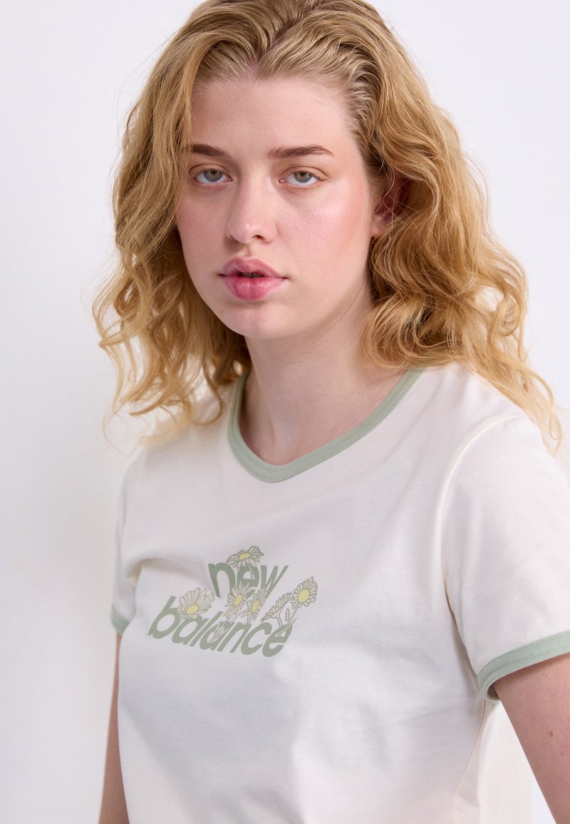 T-shirt in cotone color crema con maniche corte, colletto a coste verde e grafica floreale "new balance" in verde e giallo.