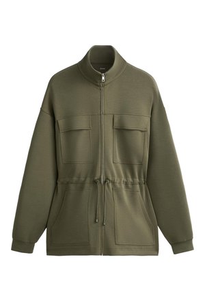Olive green zip-up jacket made of soft fabric, featuring a high neck, drawstring waist, two chest pockets, and two side pockets.
