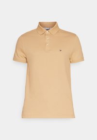 Beżowa koszulka polo wykonana z bawełny, z kołnierzykiem, trzema guzikami i małym logo na lewej piersi. Krótkie rękawy z dopasowanym krojem.