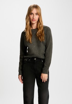 Suéter gris oscuro con cuello redondo y mangas largas, con sutiles acentos de cuentas. Combinado con jeans negros de cintura alta.