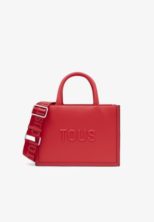 Bolso de mano de piel sintética roja con el logotipo "TOUS" en relieve, asas redondeadas dobles y strap ajustable a rayas. Textura suave, diseño estructurado.