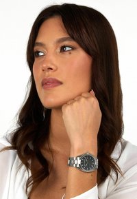 Orologio in acciaio inox argentato con quadrante nero testurizzato, caratterizzato da una cassa rotonda e un bracciale a maglie.