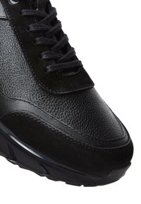 Zapatillas negras con materiales de cuero texturizado y ante, diseño de punta redonda, cordones planos y suela de goma gruesa con acentos angulares.