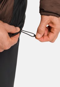 Mani che regolano l'orlo di una giacca nera con un cordino e un fermaglio su uno sfondo bianco semplice.