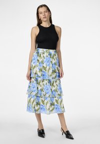 Un haut sans manches noir associé à une jupe plissée à plusieurs niveaux, ornée de motifs floraux bleus sur fond clair. Des chaussures à talons noires complètent le look.