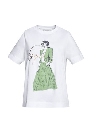 Biała koszulka z krótkim rękawem z grafiką przedstawiającą kobietę w okularach przeciwsłonecznych, zielonej kurtce i długiej zielonej spódnicy, z rękami w kieszeniach.