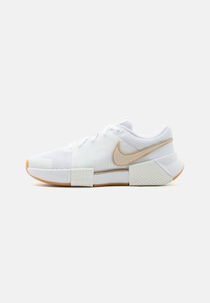 Biele nízke tenisky Nike s béžovým logom, sieťovaným zvrškom a hrubou podrážkou s geometrickými vzormi na svetlom pozadí.