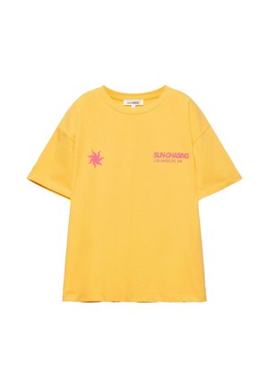 Žuta majica kratkih rukava s ružičastim sunčevim motivom i natpisom "SUN-CHASING LOS ANGELES, CA" na prednjoj lijevoj strani.