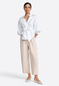 White blouse with a wrap design and puff sleeves, tied at the waist. Paired with beige wide-leg trousers and light-colored heeled shoes.