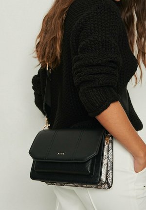 Bolso bandolera de cuero negro con una textura suave, cuenta con cierre de solapa, herrajes dorados y un lateral con patrón en gris y blanco.