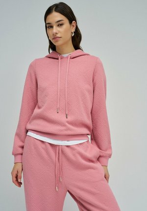 Sweat à capuche rose en tissu texturé avec un motif de logo, cordon de serrage et poignets côtelés. Associé à un pantalon de jogging texturé assorti.
