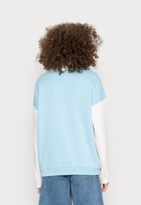 Hellblauer Pullover mit weißen und rosa Ärmeln, lockere Passform, runder Halsausschnitt und geripptem Saum. Die Rückansicht zeigt ein Farbblock-Design.