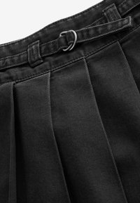 Gros plan sur un tissu noir plissé avec une ceinture noire ajustable ornée d'une boucle argentée à double anneau.