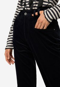Marineblauwe corduroy broek met een zachte textuur, voorzien van zijzakken en een knoopsluiting bij de taille, gecombineerd met een gestreepte lange mouw top.