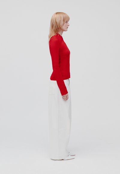 Tricou roșu cu mânecă lungă, cu un design ajustat, asortat cu pantaloni albi, largi. Ținuta are modele minime și o siluetă curată.