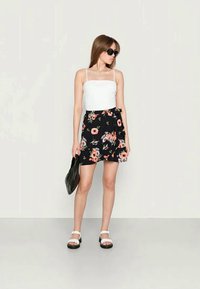 Top sem mangas branco combinado com uma saia mini floral preta com flores rosas e brancas, complementado por sandálias brancas e uma bolsa preta.