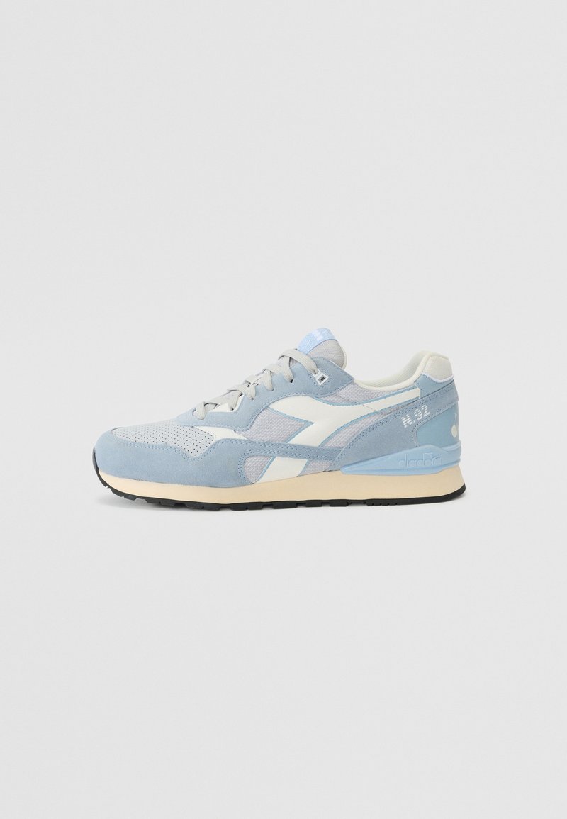 Light blue athletic shoe with mesh and suede material, white accents, rounded toe, and black rubber sole. Features lace-up closure and branding.