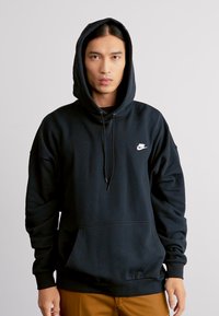Felpa nera con cappuccio e coulisse, dotata di tasca frontale, realizzata in tessuto morbido. Presenta un piccolo logo Nike bianco sul lato sinistro del petto. Design semplice.