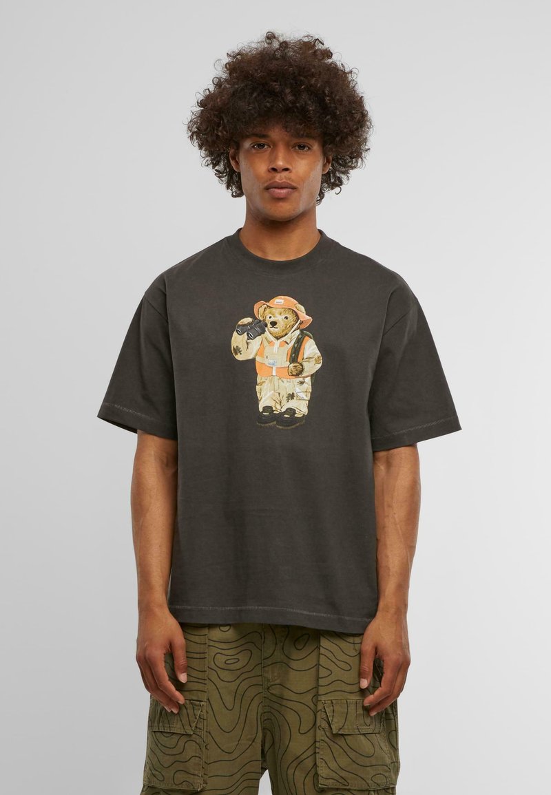 Tamsiai pilka medvilninė marškinėliai su meškos grafika, užsidėjusios oranžinę skrybėlę ir liemenę. Trumpomis rankovėmis ir laisvu kirpimu. Tekstūruotos cargo kelnės su bangų raštais.