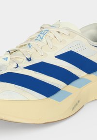 Λευκό και μπλε αθλητικό παπούτσι Adidas με τρεις μπλε ρίγες, κρεμ σόλα με την επισήμανση "Lightstrike Pro" και λευκά κορδόνια σε λευκό φόντο.