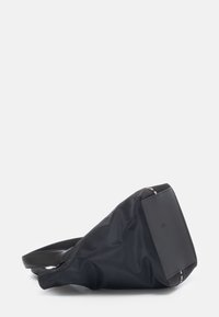 Borsa nera in nylon con un design snodato, caratterizzata da una base piatta e rettangolare e una tracolla regolabile. Dettagli con zip sui lati.