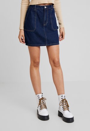 Žena nosí tmavě modrou džínovou minisukni s předními kapsami a bílé kotníkové boty na šněrování s tlustými podrážkami.