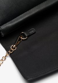 Clutch in pelle nera con texture liscia, dotato di una tracolla in catena dorata e chiusura con zip. Include un piccolo tirante in pelle.
