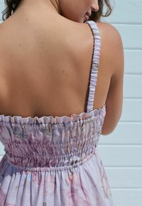 Blomsterpræget sommerkjole i lys lilla, med rynket detaljering ved livstykket og justerbare spaghetti-stropper. Glat stoftekstur.