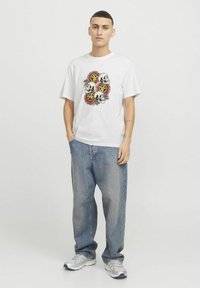 Hvid bomulds T-shirt med et farverigt grafisk print af kranier og blomster, kombineret med lyseblå baggy denimbukser og sølvfarvede sportssko.