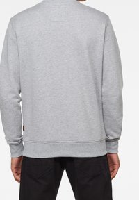 Sudadera gris con cuello redondo, puños y dobladillo acanalados. Textura suave con una pequeña etiqueta en el lado izquierdo cerca del dobladillo.