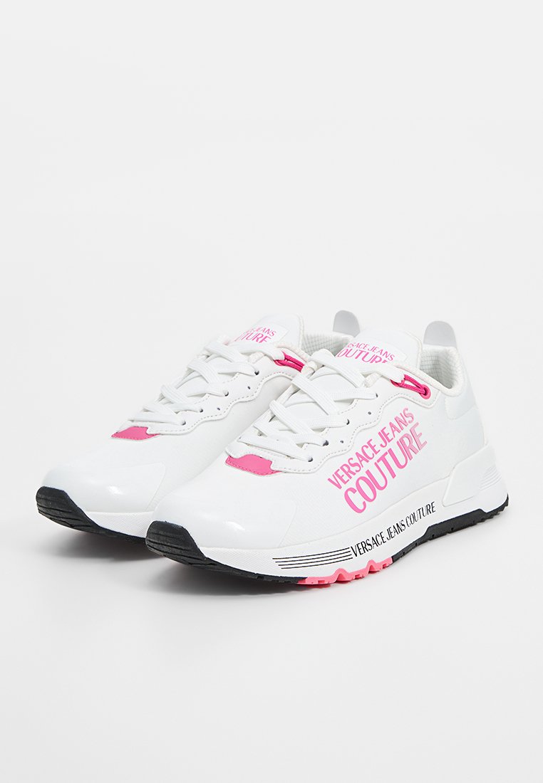 Zapatillas deportivas blancas con detalles en rosa y suela negra. Presentan la marca "VERSACE JEANS COUTURE" en el lateral y en la lengüeta. Materiales de malla y sintético.