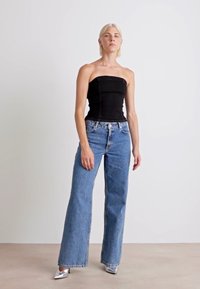 Μαύρο strapless τοπ, μπλε τζιν με ψηλή μέση και ασημένιες γόβες με μυτερή μύτη. Το μοντέλο στέκεται μπροστά σε ουδέτερο φόντο.