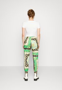 Pantalones de tela estampada en verde, negro y dorado con un diseño ajustado; llevados con una blusa blanca de manga corta y botines.