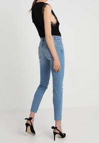 Haut noir avec bordure en dentelle, jean slim-fit bleu clair avec ourlet effiloché, et chaussures à talons hauts noires avec accents en nœud.