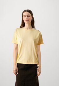 Gelbes Baumwoll-T-Shirt mit Rundhalsausschnitt, kurzen Ärmeln und seitlichen Bindebändern für eine verstellbare Passform. Weicher Stoff und lässiges Design.