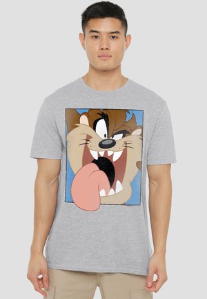 Young man wearing a light gray T-shirt featuring Taz from Looney Tunes with his mouth open and tongue sticking out.