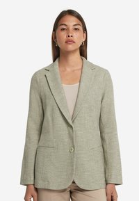 Ljusgrön texturerad blazer med en knapp, snedskurna klackar och två framfickor, tillverkad av vävt tyg.