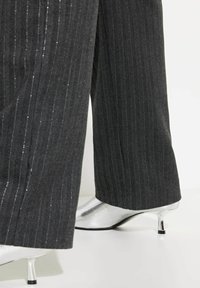 Mustat raitapaitahousut, joissa on leveä lahje, yhdistettynä kiiltäviin hopeisiin nilkkabootseihin, joissa on kapea korko ja musta yksityiskohta kannan juurella.