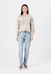 Pull en tricot avec des rayures horizontales multicolores, col rond et manches longues, associé à un jean droit bleu clair avec des détails usés.