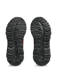Semelles de chaussures en caoutchouc noir avec des motifs de traction profonds, présentant des textures et des rainures surélevées pour une meilleure adhérence. Des accents rouges sont visibles sur les bords.