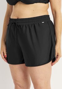 Svarta badshorts med elastisk midja, snörning och sidslitsar för rörlighet. Tillverkade av mjukt, lätt material.