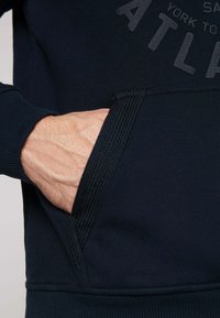 Sudadera marina con un bolsillo canguro, puños acanalados y un detalle de logo texturizado. Tejido suave con un acabado liso y un ajuste relajado.