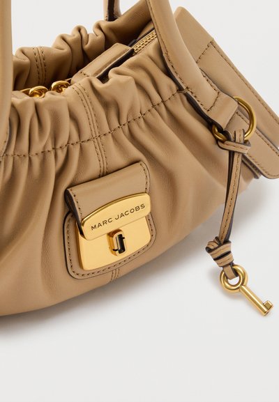 Μπεζ δερμάτινη τσάντα χειρός Marc Jacobs με συγκεντρωμένες λεπτομέρειες, χρυσό κούμπωμα και διακοσμητικό χρυσό κλειδί προσαρτημένο σε δερμάτινο λουράκι.