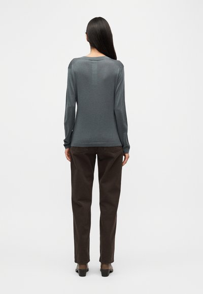 Μπλούζα με μακριά μανίκια σε γκρι χρώμα, με στρογγυλή λαιμόκοψη, συνδυασμένη με σκούρο καφέ παντελόνι φαρδιάς γραμμής. Το ύφασμα φαίνεται απαλό· ελάχιστες εμφανείς ραφές και λεπτομέρειες.