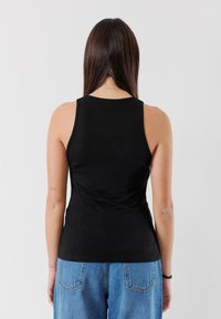 Top senza maniche nero realizzato in tessuto morbido, design aderente e scollatura rotonda. Indossato con jeans a vita alta blu chiaro.