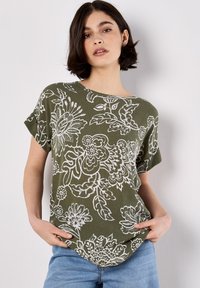 Top de manga corta color verde oliva con un patrón floral blanco, escote redondo y dobladillo curvado, fabricado con un material suave y texturizado.